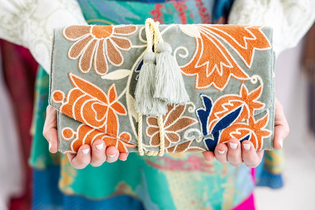 Handmade clutch with floral patterns and tassels held by a person.