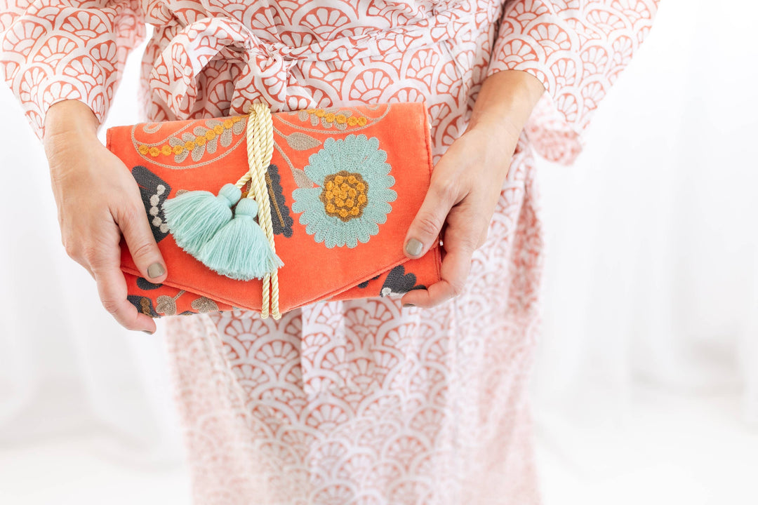 Person holding a colorful clutch with floral design and tassels against a light background