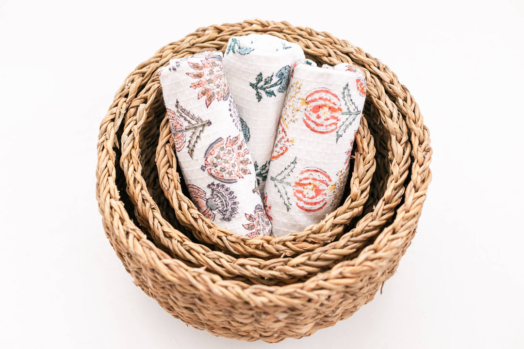 Set of floral-patterned baby blankets in a woven basket on a white background